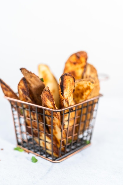 Spicchi di patate appena sfornati con spezie in un cestello di filo metallico.