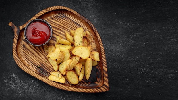 Spicchi di patate fritte con ketchup su una tavola di legno su uno sfondo scuro