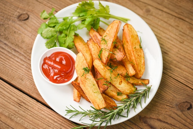 Spicchi di patate su piatto bianco con coriandolo alle erbe di rosmarino e salsa di ketchup Cottura di patatine fritte o patate fritte