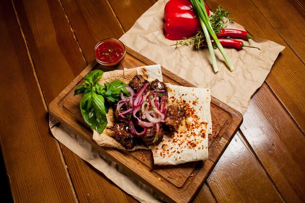 Spiedini di agnello al sugo, con cipolle, lavash. Turco e arabo - Kebab tradizionale orientale con verdure, cipolle, pomodori, peperoni, pane pita e lattuga su uno sfondo di legno.