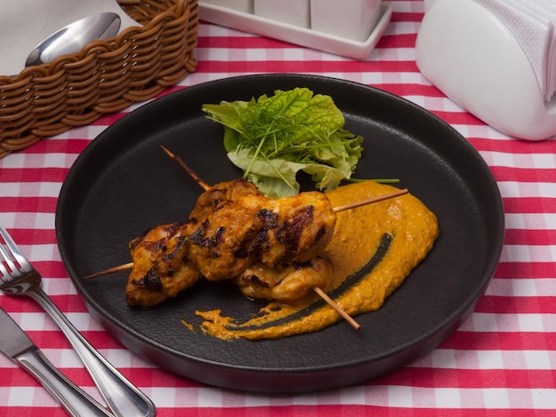 Spiedini di pollo saporiti con curry su un piatto nero