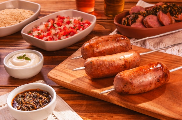 Spiedini di salsiccia di maiale alla griglia barbecue sul tagliere di legno con chimichurri