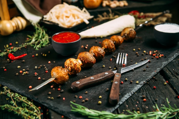 Spiedini di shashlyk di kebab di funghi appetitosi con salsa rossa e cipolla sottaceto su una tavola nera su uno sfondo di legno scuro