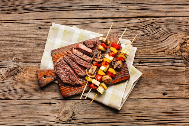 Spiedo di carne e fetta di bistecca fritta sul tagliere di legno