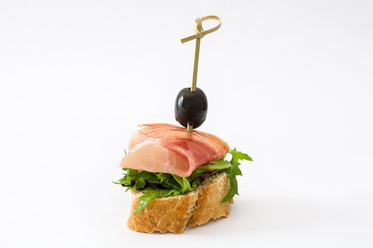 Foto spiedo spagnolo del prosciutto di serrano delle fette sottili con oliva e lattuga isolate su superficie bianca