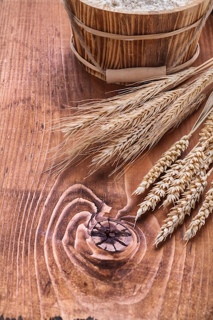 Spighe di grano con secchio di farina sulla vecchia tavola di legno