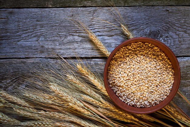 Spighe di grano e una ciotola di grano su una tavola di legno scuro