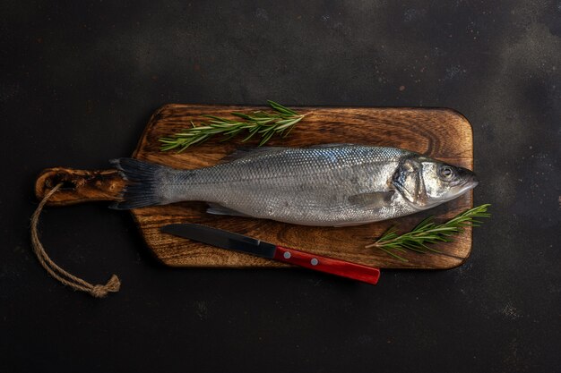 Spigola fresca di pesce con rosmarino e coltello sulla tavola nera