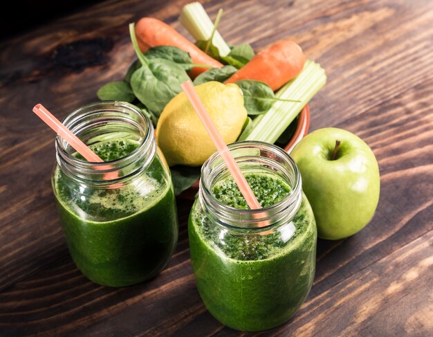 Spinaci con succo di mela e verdure un barattolo di bibite con paglia sul tavolo di legno