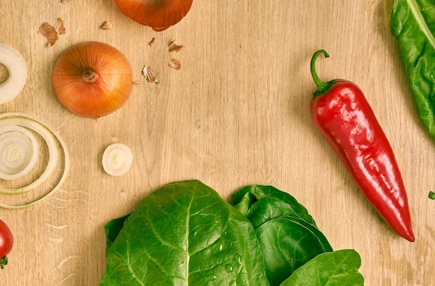 Spinaci freschi, peperoncino, cipolla, pomodorini ed erbe verdi su un bancone da cucina in legno.