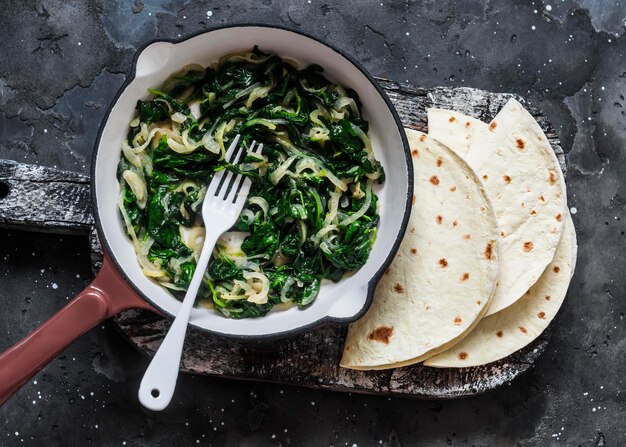 Spinaci stufati in padella e tortillas su uno sfondo scuro vista dall'alto