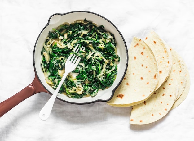 Spinaci stufati in una padella e tortillas su uno sfondo chiaro vista dall'alto