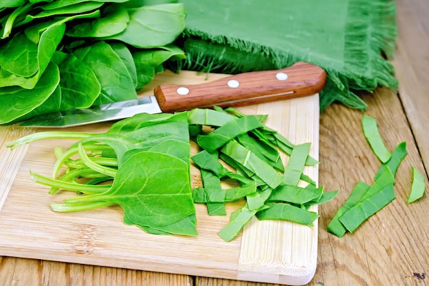 Spinaci verdi tagliuzzati, coltello e tovagliolo su uno sfondo di assi di legno