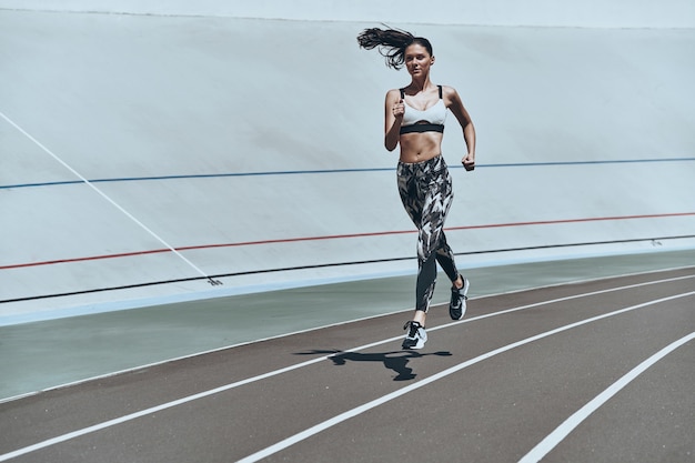 Spingere forte. Per tutta la lunghezza della giovane donna in abbigliamento sportivo che fa jogging mentre si esercita all'aperto