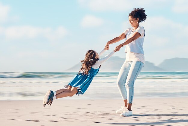 Spinning madre e un bambino felice in spiaggia durante una vacanza in famiglia o un'avventura Una giovane donna o mamma e bambina che giocano insieme mentre sono all'aperto per divertirsi in estate e viaggiare nella natura