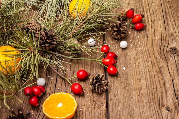 Spirito di Natale sul tavolo di legno. Mandarini freschi, bacche di rosa canina, caramelle, rami e coni di pino, neve artificiale