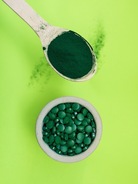 Spirulina hawaiana verde in cucchiai di pillole e polvere su sfondo verde chiaro