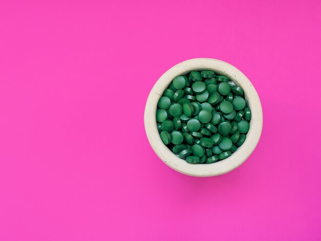 Spirulina hawaiana verde in cucchiai di pillole su sfondo rosa Super cibo sano stile di vita