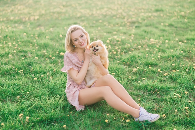 Spitz attraente del cane della tenuta della giovane donna fuori e sorridere alla macchina fotografica, camminante nel parco.