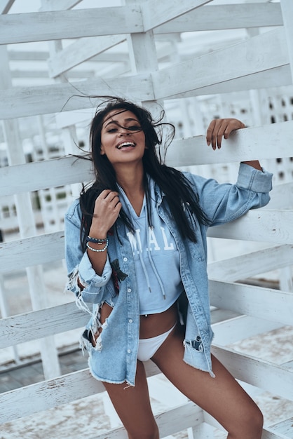 Splendida bellezza. Attraente giovane donna di razza mista in camicia di jeans che sorride mentre sta in piedi all'aperto