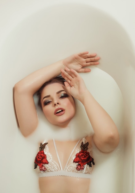 Splendida donna bionda in lingerie di pizzo con ricami fa un bagno con il latte