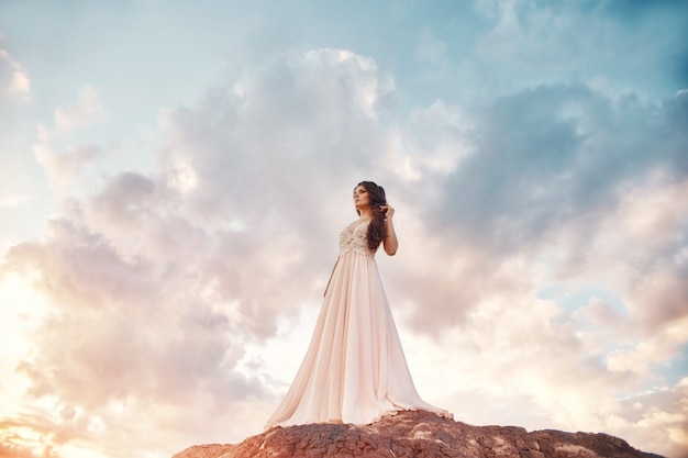 Splendida donna bruna in montagna al tramonto e cielo blu con nuvole.