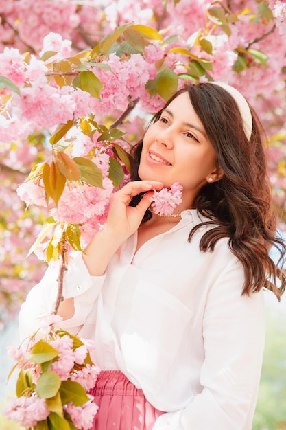 Splendida donna caucasica gentile sotto lo spazio di copia dell'albero di sakura rosa in fiore