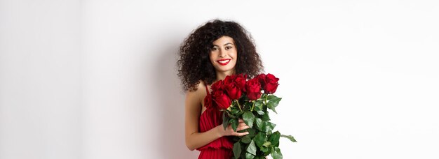 Splendida donna caucasica in abito da sera rosso che riceve bouquet di fiori ragazza con rose rosse smili