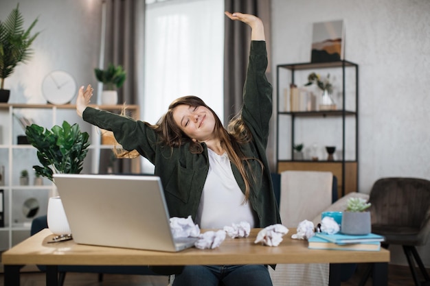 Splendida donna d'ufficio che si rilassa allungando il corpo mentre è seduta davanti al suo computer portatile