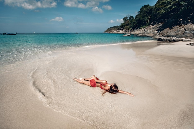 Splendida donna dai capelli rossi con un corpo sexy vestito in bikini rosso e occhiali da sole sdraiato sulla spiaggia, donna seducente in costume da bagno resto dopo il nuoto. Phuket. Tailandia