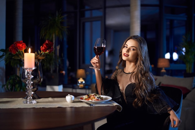Splendida donna in abito nero con in mano un bicchiere di vino rosso