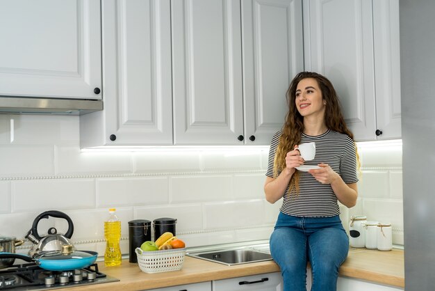 Splendida donna rilassarsi mattina in cucina e bere un caffè. Comodo tempo libero a casa.