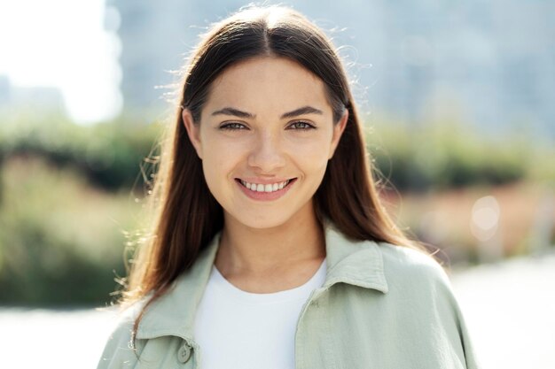 Splendida donna sorridente con capelli lunghi castana che guarda l'obbiettivo in piedi nel parco