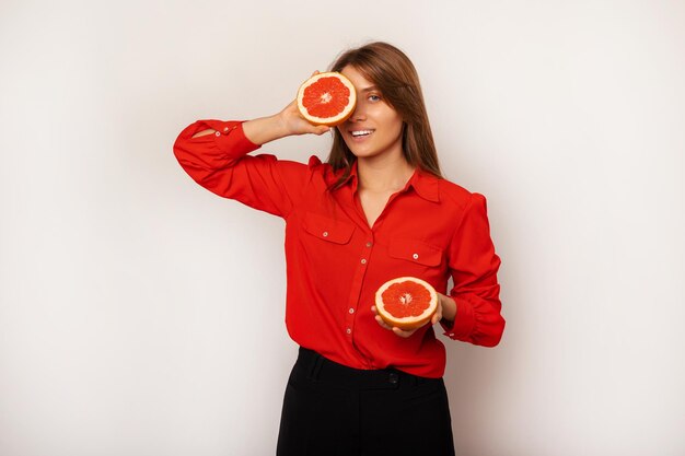 Splendida giovane donna bionda che indossa una camicia rossa tiene in mano le metà del pompelmo