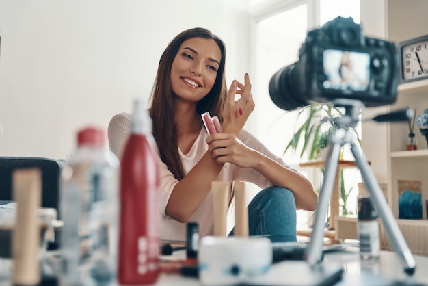 Splendida giovane donna che applica lucidalabbra e sorride mentre realizza video sui social media