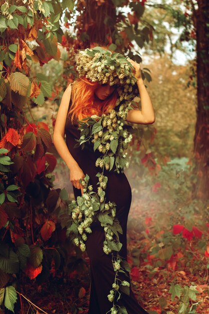 Splendida giovane signora dai capelli rossi con il luppolo in posa all'aperto nella foresta