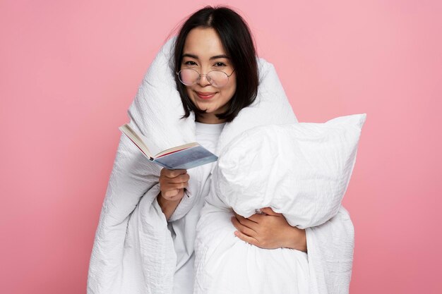 Splendida ragazza che abbraccia cuscino e legge un libro interessante al mattino