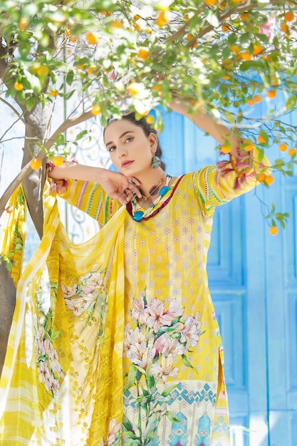 Splendida ragazza in piedi sotto l'albero arancione che indossa un vestito giallo Desi