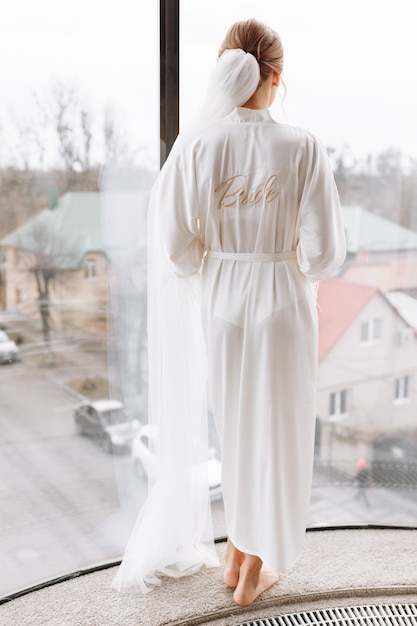 Splendida sposa. bella donna con i capelli lunghi in una veste bianca alla finestra.