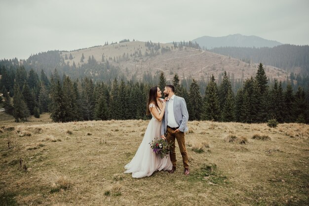 Splendide coppie in viaggio di nozze che abbracciano in montagna di verde pineta sullo sfondo.