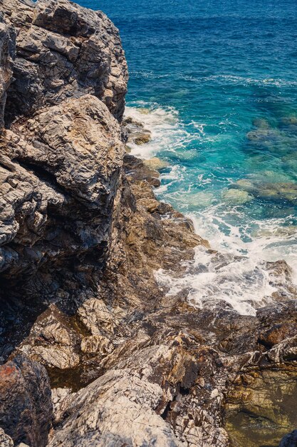 Splendide viste sul blu del Mar Mediterraneo Onde di rocce soleggiate con schiuma e spruzzi d'acqua L'onda si schianta contro le rocce sulla riva