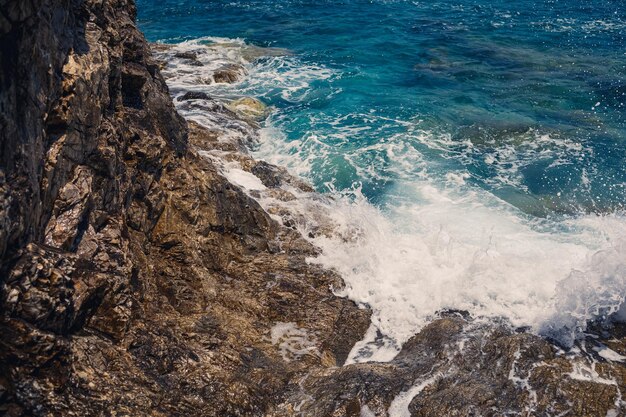 Splendide viste sul blu del Mar Mediterraneo Onde di rocce soleggiate con schiuma e spruzzi d'acqua L'onda si schianta contro le rocce sulla riva