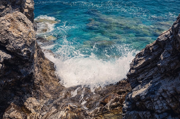 Splendide viste sul blu del Mar Mediterraneo Onde di rocce soleggiate con schiuma e spruzzi d'acqua L'onda si schianta contro le rocce sulla riva