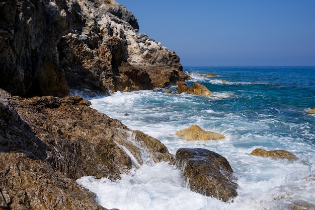 Splendide viste sull'azzurro Mar Mediterraneo. Rocce soleggiate, onde con schiuma e spruzzi d'acqua. L'onda si infrange sugli scogli sulla riva