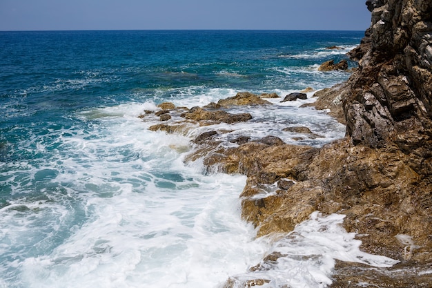 Splendide viste sull'azzurro Mar Mediterraneo. Rocce soleggiate, onde con schiuma e spruzzi d'acqua. L'onda si infrange sugli scogli sulla riva