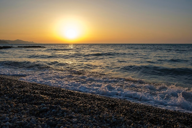 Splendido paesaggio al tramonto sul mare Specchio riflesso dell'alba su ciottoli bagnati Luce solare dorata sulle onde del mare Primo piano della marea e della costa di ciottoli del mare