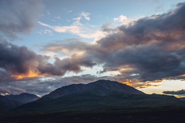 Splendido scenario di montagna con luce dorata dell'alba nel cielo nuvoloso. Paesaggio montano panoramico con colori illuminanti nel cielo al tramonto. Siluette delle montagne all'alba. Luce solare che illumina l'oro nel cielo