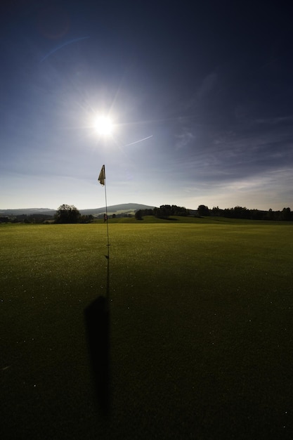 Splendido scenario di una buca da golf e una bandiera in un campo contro uno sfondo luminoso giorno di sole