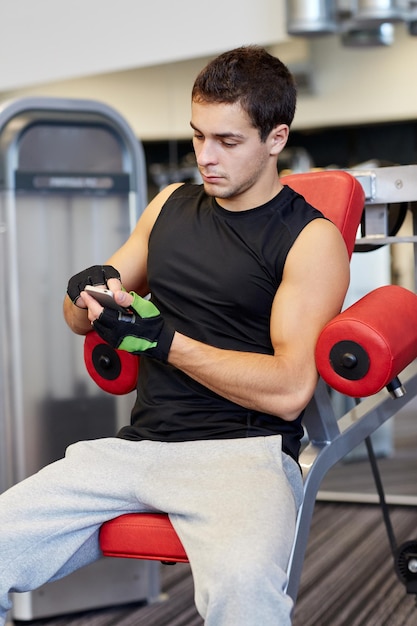 sport, bodybuilding, stile di vita, tecnologia e concetto di persone - giovane con smartphone in palestra