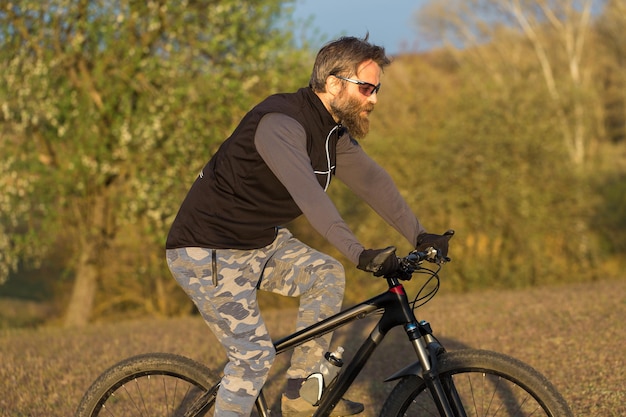 Sport brutale ragazzo barbuto su una moderna mountain bike Ciclista sulle verdi colline in primavera